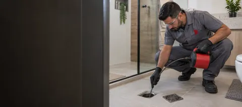 Profissional inspecionando um ralo de piso em banheiro